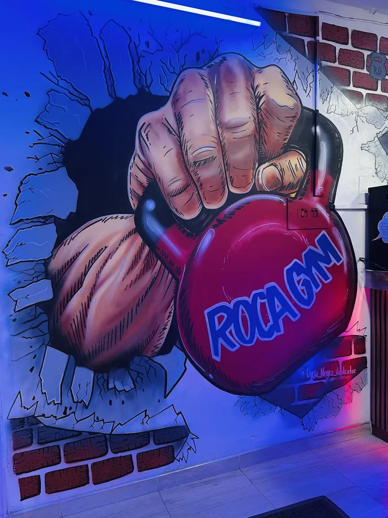 Mural pintado en el local: un puño rompe una pared de ladrillo y sostiene la pesa rusa de Roca Gym.